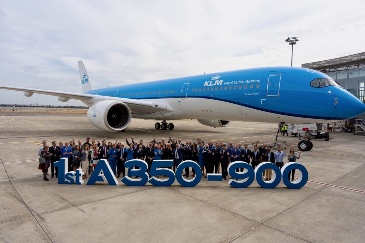 Group of people posing in front of a blue KLM Airbus A350 900 on the tarmac celebrating the first delivery with a large display reading 1st A350 900 in the foreground