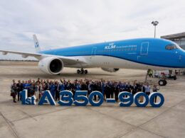 Group of people posing in front of a blue KLM Airbus A350 900 on the tarmac celebrating the first delivery with a large display reading 1st A350 900 in the foreground