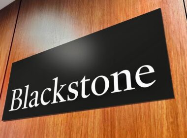 Tilted black sign on a wooden surface displaying the white word Blackstone in serif letters close up