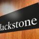 Tilted black sign on a wooden surface displaying the white word Blackstone in serif letters close up