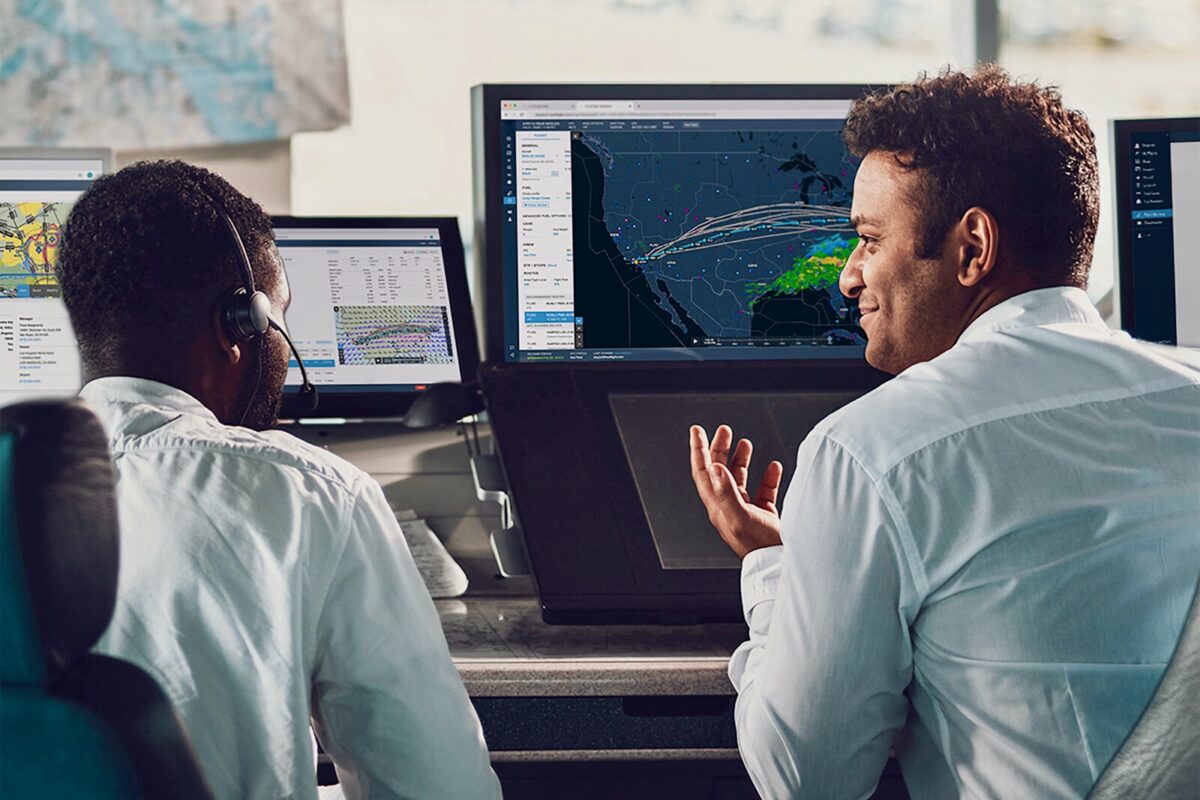 Recently Saved 1 of 1 34 Two operators in a control room monitor a large digital map showing weather patterns and routes on a central screen one gesturing as they discuss data