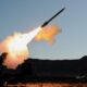 Ground based missile launcher fires a rocket bright flame and smoke plume streaking into the sky with desert terrain in the background