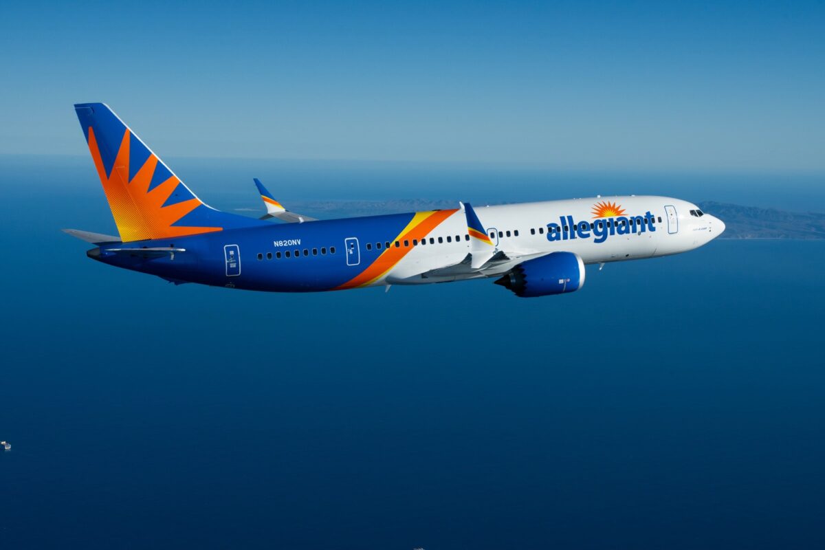 Recently Saved 1 of 1 5 Side view of an Allegiant Air Boeing 737 in blue orange and white livery flying over the ocean with distant coastline