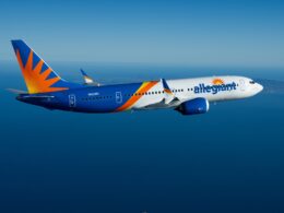 Side view of an Allegiant Air Boeing 737 in blue orange and white livery flying over the ocean with distant coastline