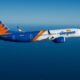 Side view of an Allegiant Air Boeing 737 in blue orange and white livery flying over the ocean with distant coastline