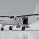 White high wing single engine utility airplane with an open side door and fold out stairs on a glossy hangar floor area