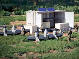 White shipping container shelter with solar panels on top crates outside and soldiers in camouflage gear in a grassy field military equipment in a training area
