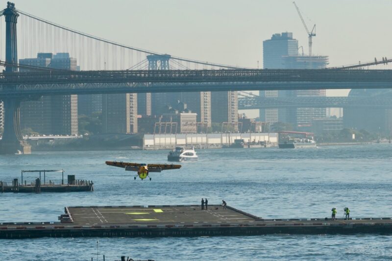 Seaplane taking off from a river with city bridges and skyscrapers in the background