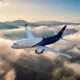 Boeing Business Jets airplane flying above clouds over mountain range at sunrise