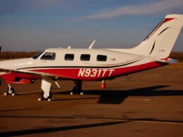 Side view of a white and red Piper private airplane with tail number N931TT parked on an airport tarmac gear down sunny day