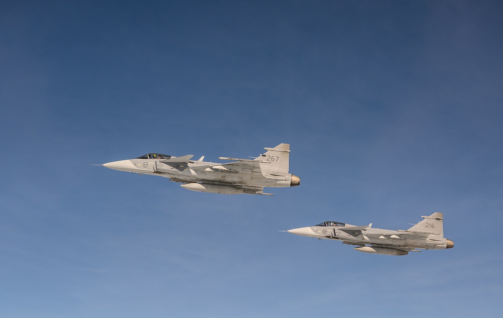 Swedish Air Force JAS 39 Gripen fighters during a NATO air policing deployment in Poland Two gray fighter jets fly in formation against a clear blue sky with 267 and 216 markings visible on the tails