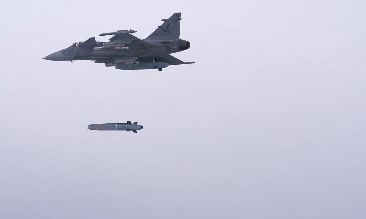 Swedish Air Force JAS 39 Gripen releases a Taurus KEPD 350 cruise missile during a test at the Vidsel Test Range Two military aircraft in flight a fighter jet releases a long cylindrical ordnance with fins beneath it against a gray sky