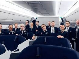 Group of flight attendants in uniform posing together inside an airplane cabin for a crew photo