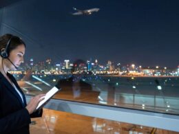 Businesswoman wearing a headset looking at a tablet in a glass walled airport lounge at night with city lights outside