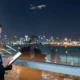 Businesswoman wearing a headset looking at a tablet in a glass walled airport lounge at night with city lights outside