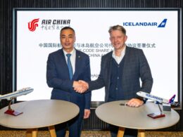 Two men in suits shake hands in front of a signage with Air China and Icelandair logos model airplanes on round tables nearby