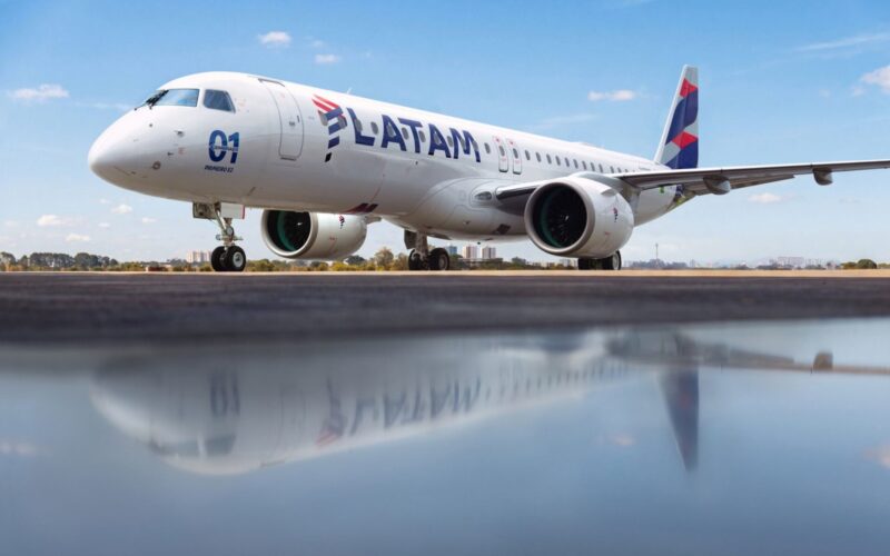 LATAM Brazil takes first E195 E2 to broaden domestic network Side view of a white LATAM commercial jet on a runway under a blue sky engines visible and reflection on the wet tarmac nearby