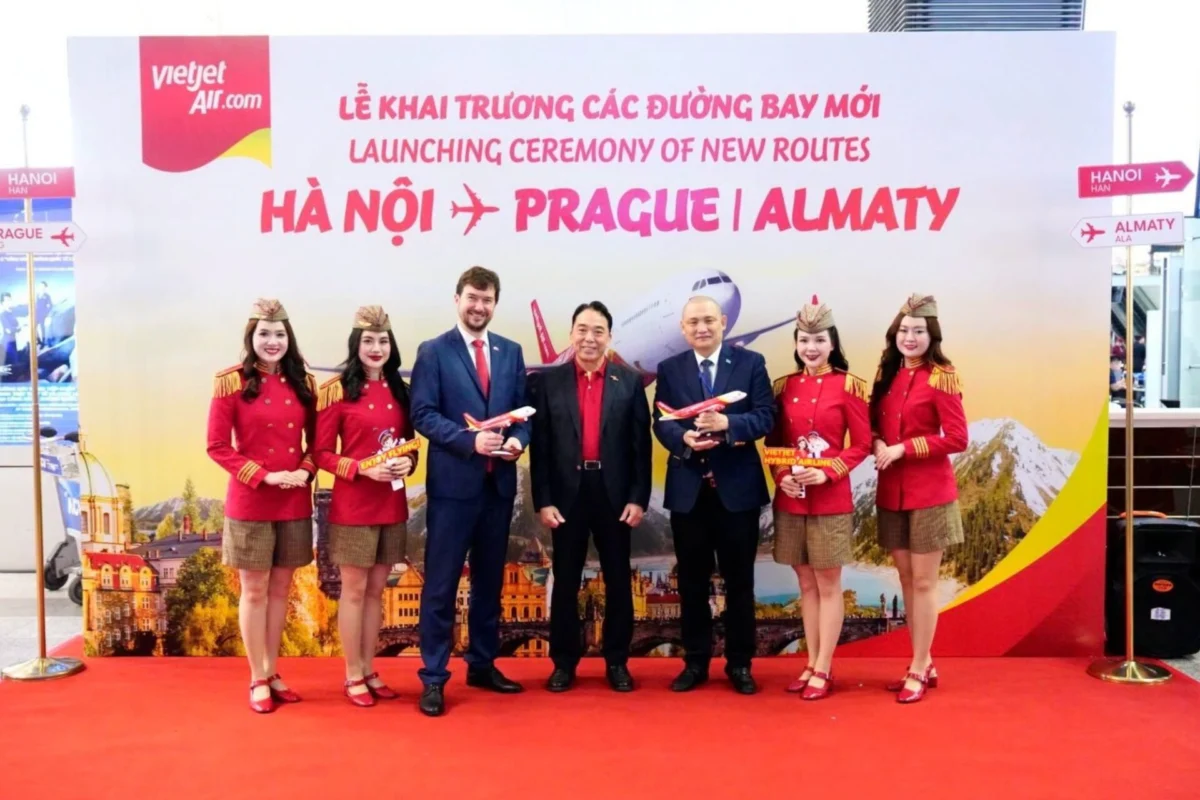 Vietjet enters EU market with HanoiAlmatyPrague routes Six people stand on a red carpet in front of a banner for VietJet Airs new routes HanoiPragueAlmaty four flight attendants in red uniforms and hats flank two men in suits each holding a model airplane
