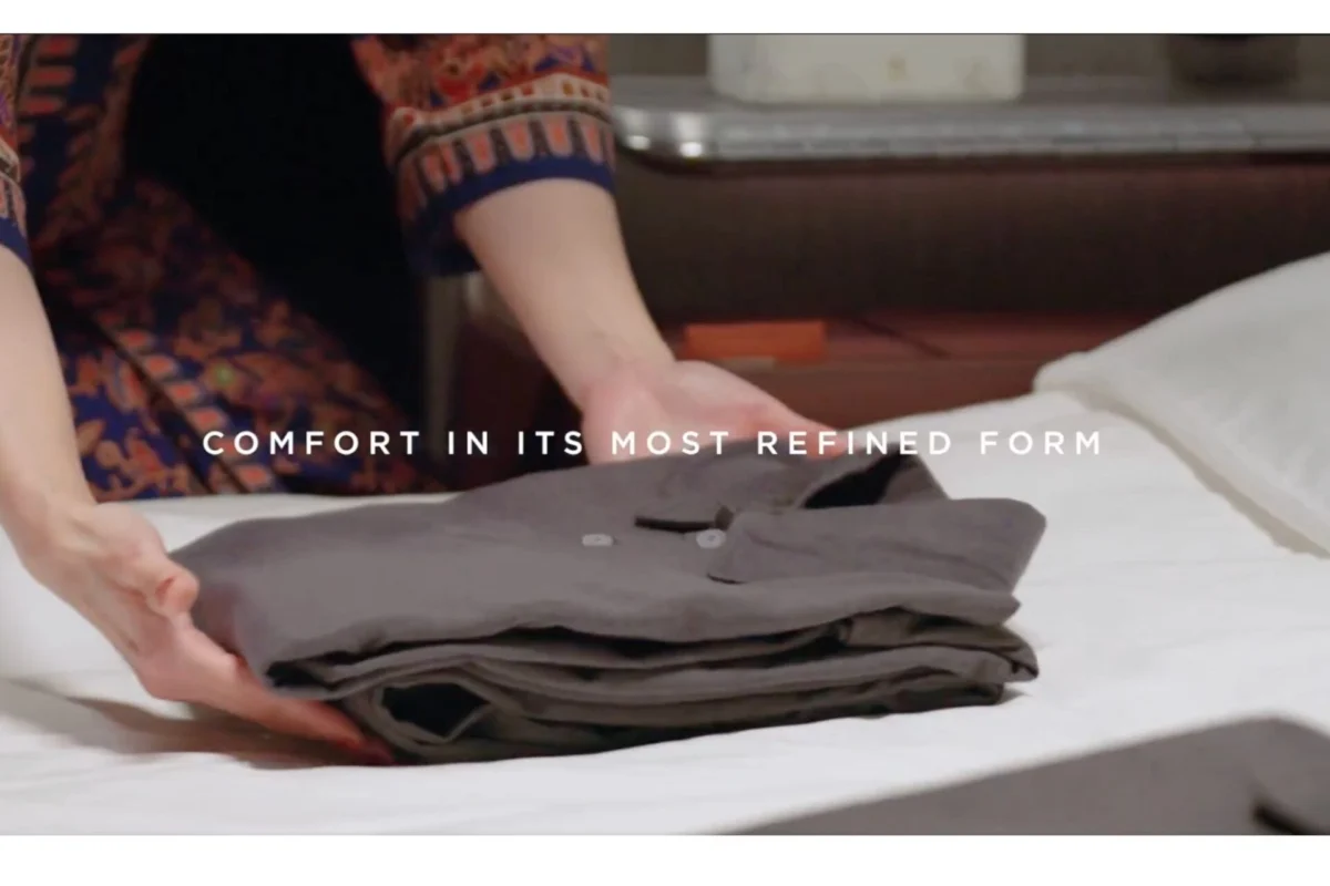 Singapore Airlines refreshes amenity kits across all classes Folded gray garments on a bed with a person folding in the background text overlay reads Comfort in its most refined form