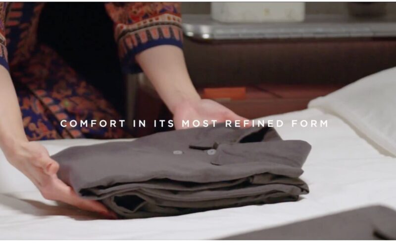 Singapore Airlines refreshes amenity kits across all classes Folded gray garments on a bed with a person folding in the background text overlay reads Comfort in its most refined form