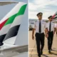 Left close up of an airplane tail with green red white and black livery airline logo visible against a blue sky right four uniformed pilots walking on the tarmac with an aircraft in the background
