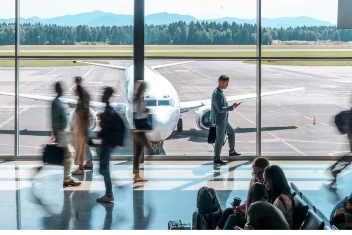 SITA agrees to buy Collins Aerospaces airport tech business Airport gate area a plane parked at the jet bridge as passengers walk with luggage outside the glass walls mountains in the distance
