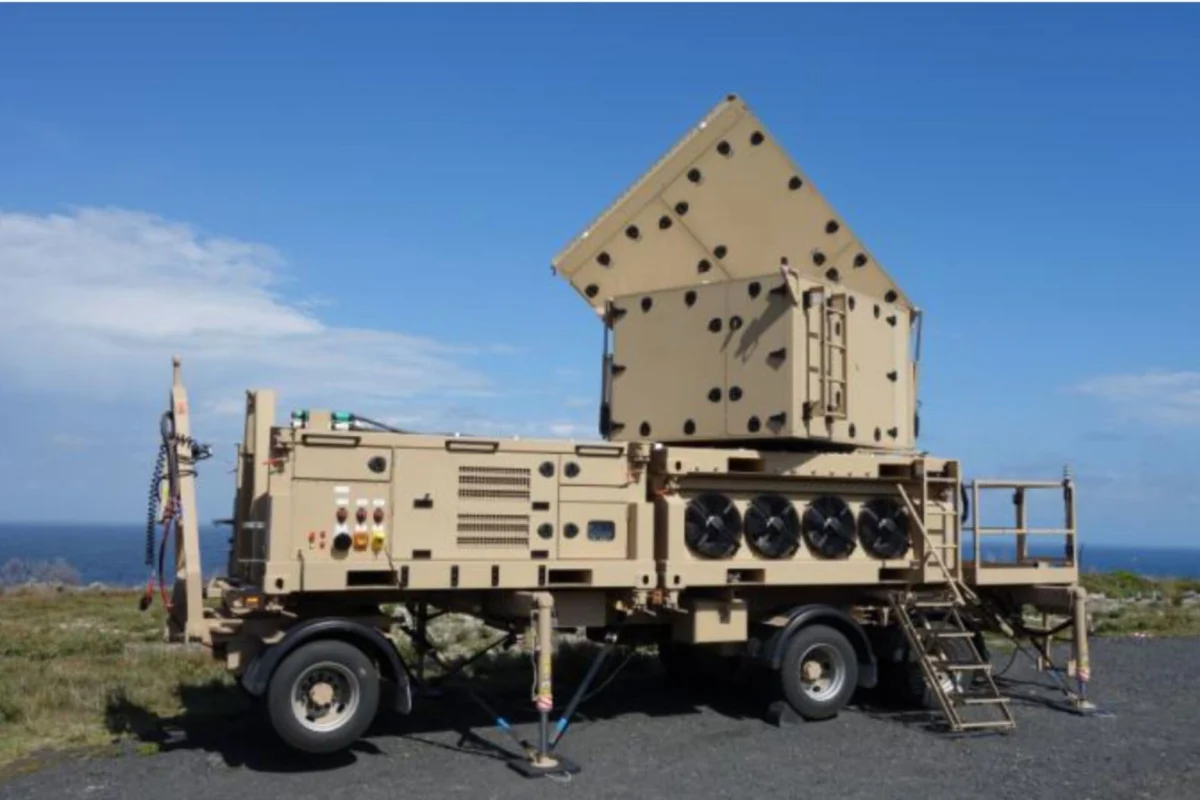 Beige mobile military radarcommunications unit on a trailer with a pyramid shaped perforated top outdoors by the coast