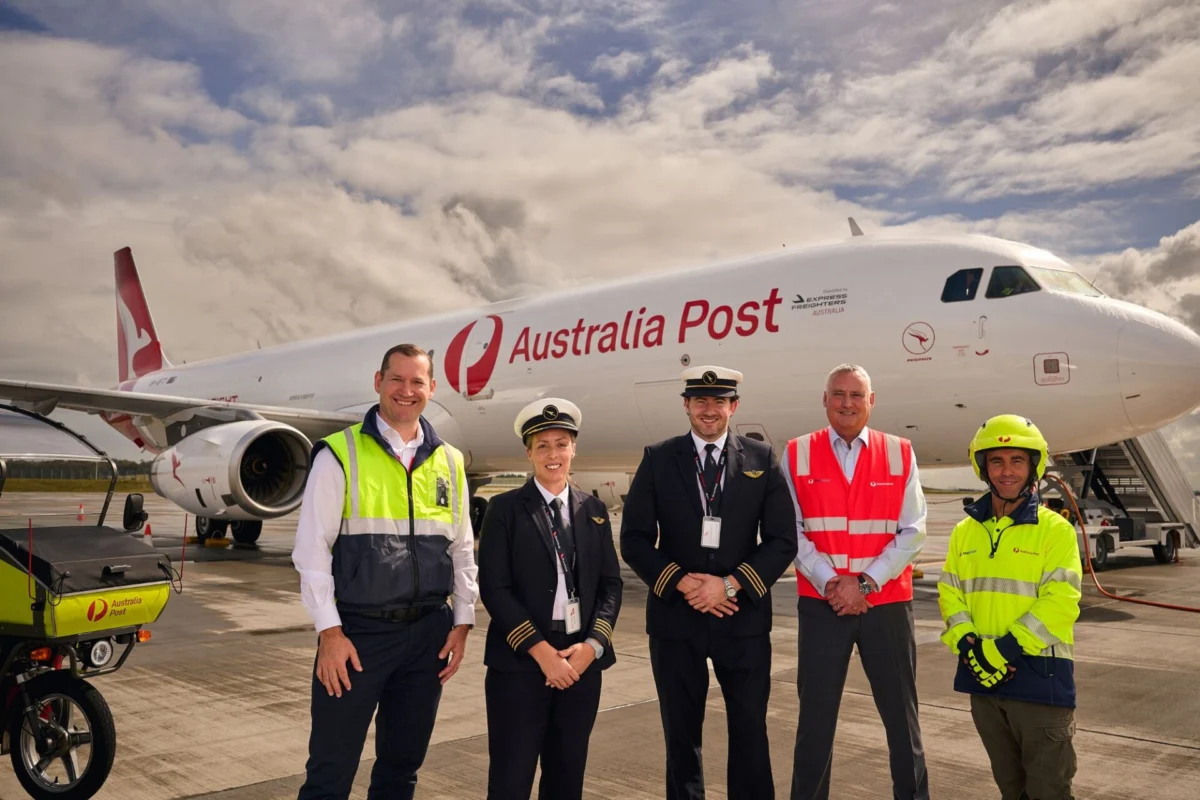 Qantas Freight takes first of three A321s for Australia Post Group of Australia Post staff in uniform posing in front of a large white Australia Post airplane on the tarmac