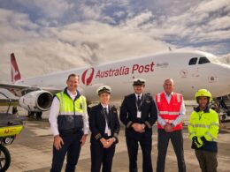 Group of Australia Post staff in uniform posing in front of a large white Australia Post airplane on the tarmac