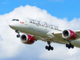 Commercial jet in ascent with two red engines nose forward against a blue sky with clouds
