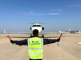 Ground crew member in a neon safety vest directs a small jet on the tarmac using signal batons