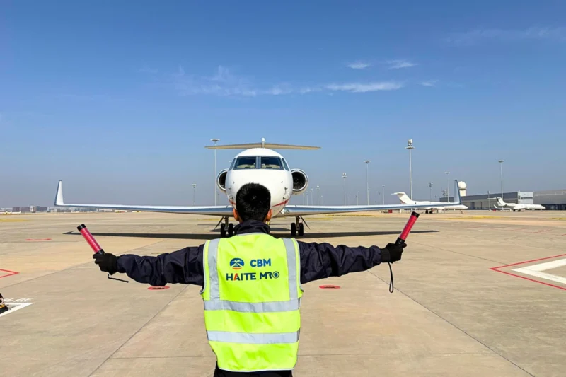 Ground crew member in a neon safety vest directs a small jet on the tarmac using signal batons