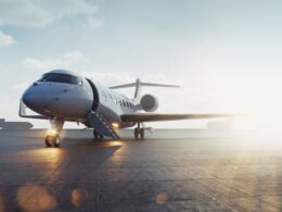 Private jet parked on a sunlit airport tarmac with boarding stairs attached to the door and jet engines visible to the side