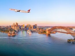 Airplane soaring above Sydney harbor with the Opera House and Harbour Bridge at sunset Qatar plane visible