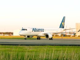 White Alliance airliner taxiing on the airport taxiway with a blue tail and yellow logo other planes in the background