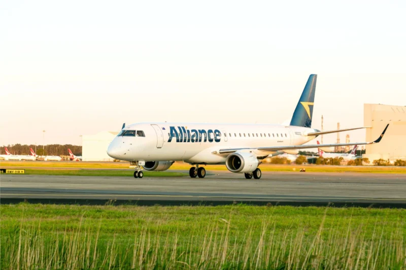 White Alliance airliner taxiing on the airport taxiway with a blue tail and yellow logo other planes in the background