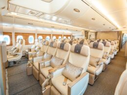 Wide view of a premium airplane cabin with beige leather seats wood paneled walls and overhead storage panels