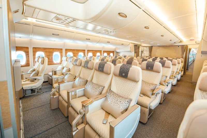 Wide view of a premium airplane cabin with beige leather seats wood paneled walls and overhead storage panels