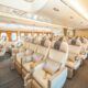 Wide view of a premium airplane cabin with beige leather seats wood paneled walls and overhead storage panels