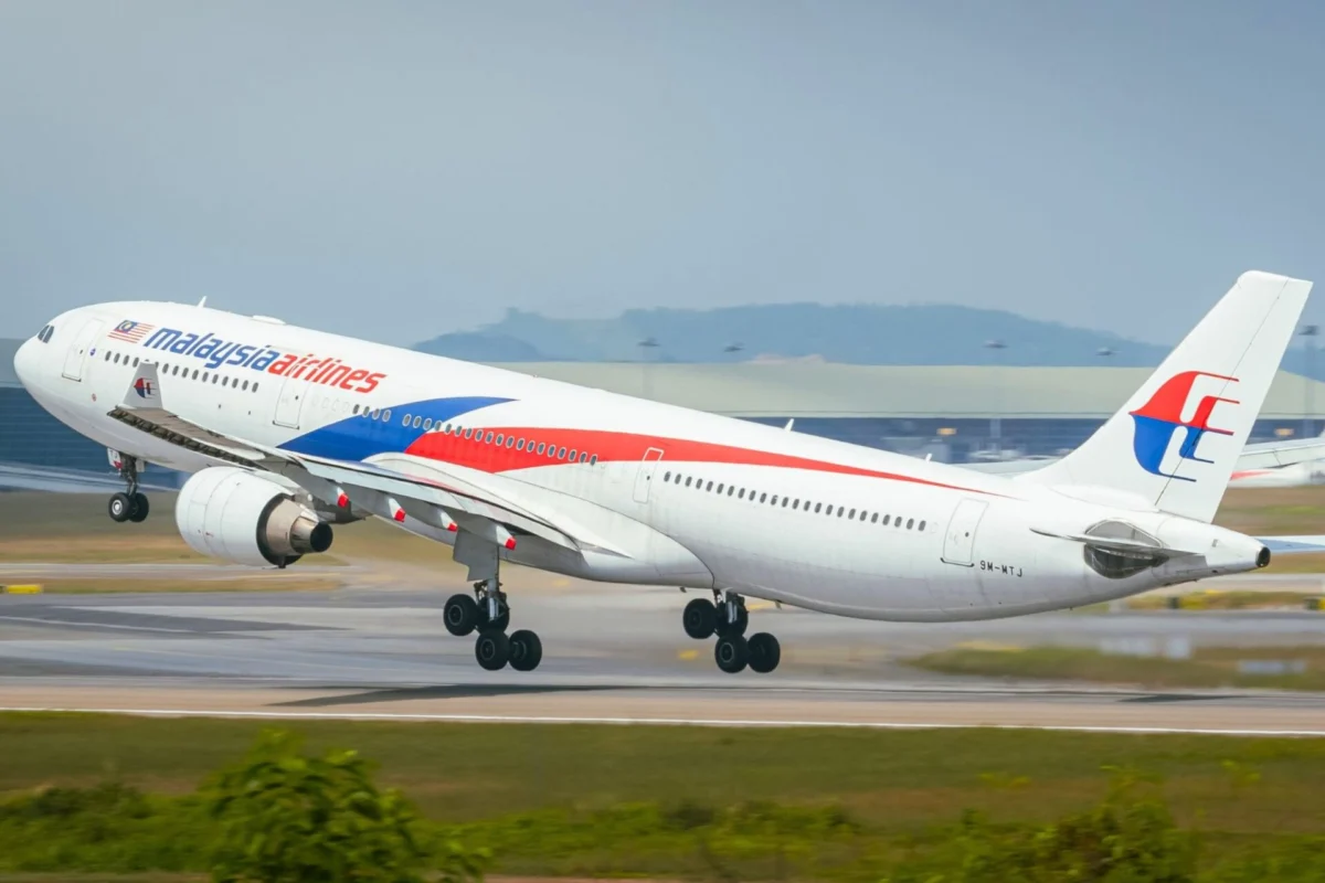 Malaysia Airlines jet taking off from a runway blue and red branding visible on the fuselage and tail