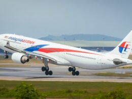 Malaysia Airlines jet taking off from a runway blue and red branding visible on the fuselage and tail
