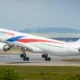 Malaysia Airlines jet taking off from a runway blue and red branding visible on the fuselage and tail