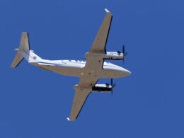 Bottom up view of a white twin engine propeller airplane flying against a clear blue sky