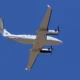 Bottom up view of a white twin engine propeller airplane flying against a clear blue sky