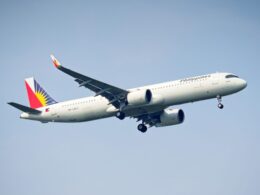White passenger jet labeled Philippines climbs into a clear blue sky tail adorned with a colorful sun flag