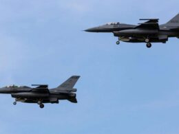 Two gray military fighter jets in formation with landing gear down against a blue sky tail numbers 6827 and 6628 visible
