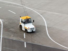 Small white airport tug with an orange roof driving on a concrete apron with curved white taxiway lines behind it