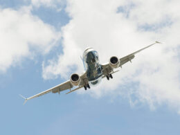 Airliner photographed from below with landing gear down flying overhead against a cloudy blue sky