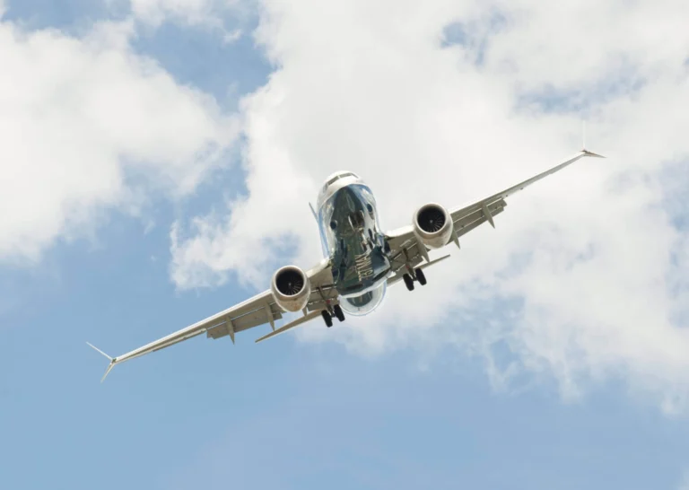 Airliner photographed from below with landing gear down flying overhead against a cloudy blue sky