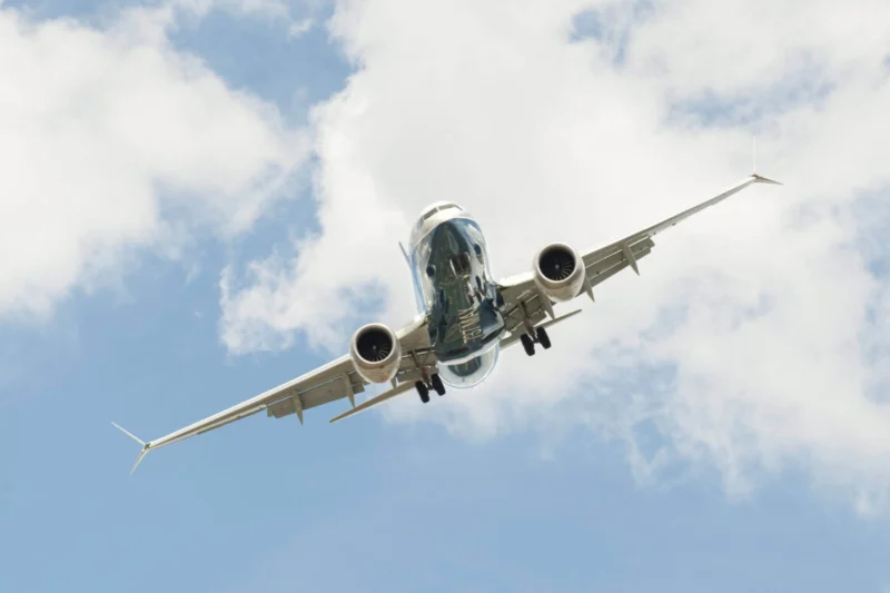 Airliner photographed from below with landing gear down flying overhead against a cloudy blue sky
